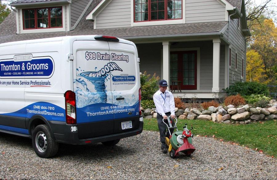 Thornton & Grooms plumber wearing branded shirt and hat next to service van with logo on it