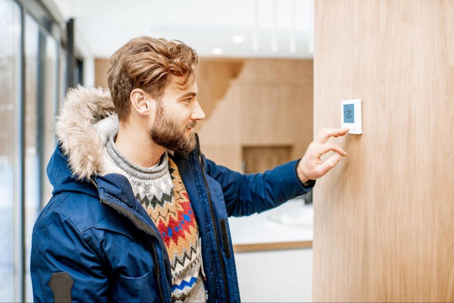 Man wearing a blue jacket with a furry hood and a multi-colored sweater changing his thermostat’s temperature