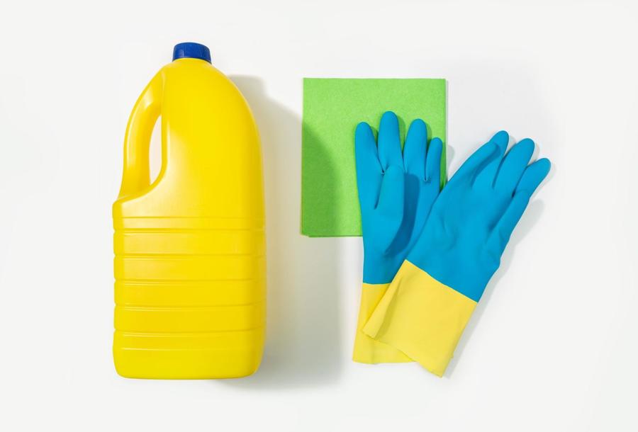Large bright yellow plastic bottle laying next to a bright green, small washcloth and a pair of blue and yellow rubber gloves