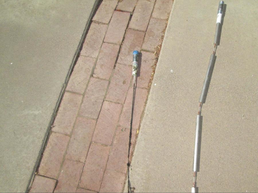 An old anode rod lying on a brick path next to a new anode rod.