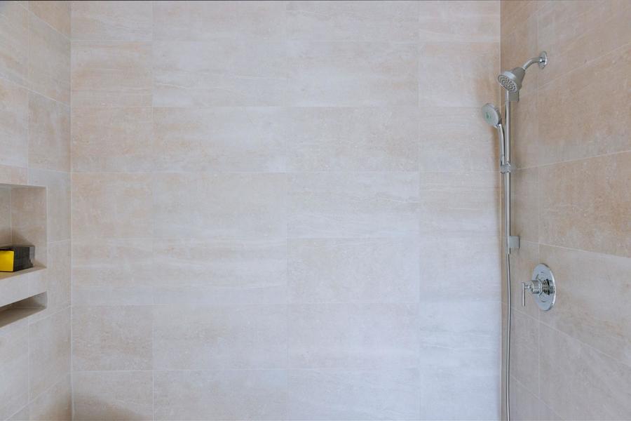Spacious beige marble shower with silver fixtures and a built shelf