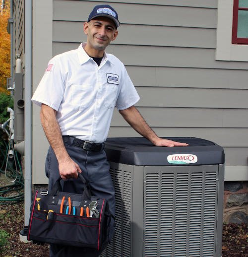 Thornton & Grooms uniformed tech smiling at the camera while holding a tool bag and leaning on a Lennox AC unit.